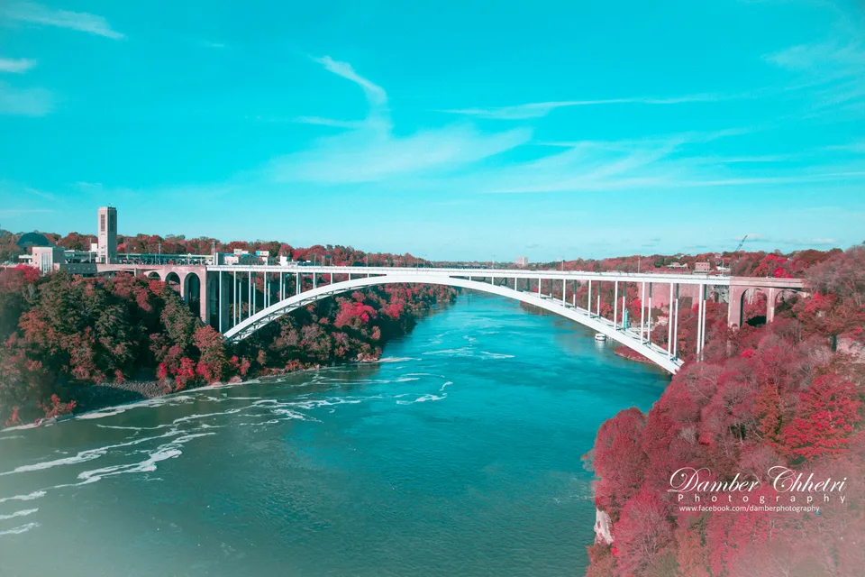 An arched bridge over a river framed by colourful trees